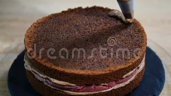 不可辨认的女性糕点厨师在厨房的开胃层蛋糕上挤压巧克力奶油视频的预览图