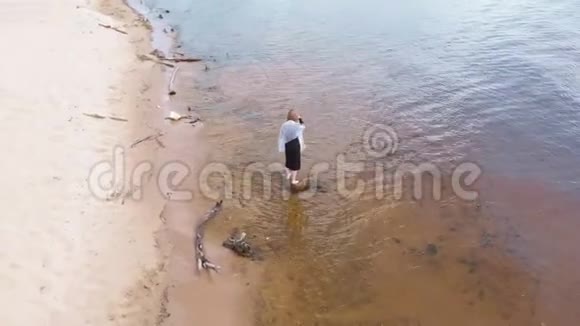 一个穿着连衣裙的年轻女子沿着海滩奔跑空中射击视频的预览图