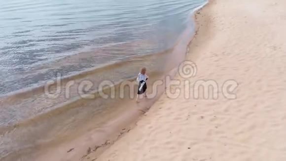 一个穿着连衣裙的年轻女子沿着海滩奔跑空中射击视频的预览图