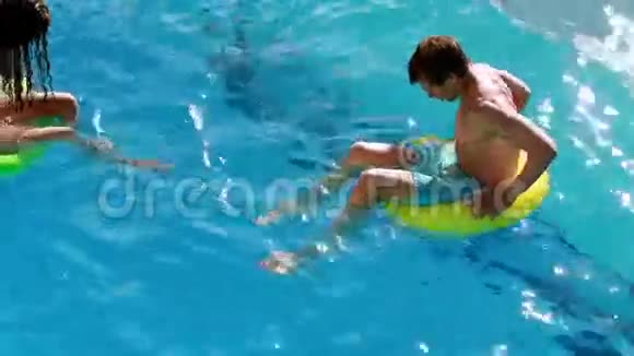 一对夫妇坐在游泳池里的充气戒指上视频的预览图