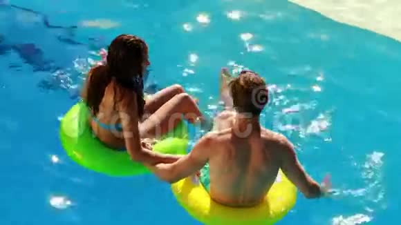 一对夫妇坐在游泳池里的充气戒指上视频的预览图