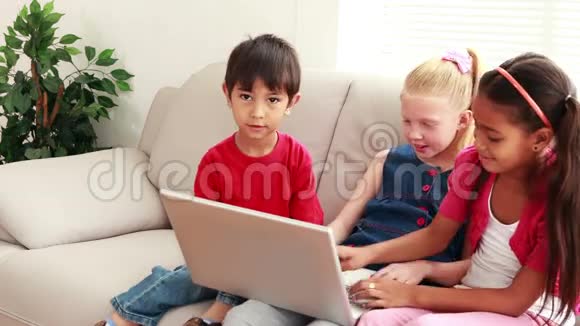 三个可爱的孩子一起在沙发上用笔记本电脑视频的预览图