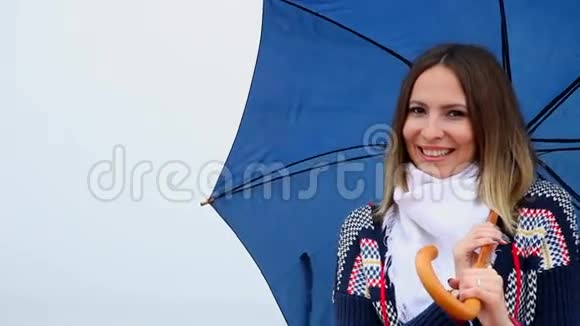 带着蓝色雨伞微笑的年轻女子眨眼视频的预览图