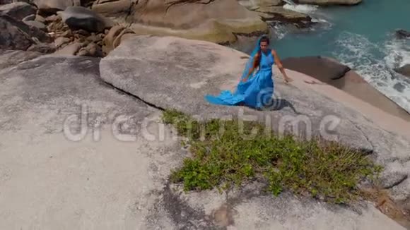 空中无人机观景女穿着蓝色连衣裙在悬崖部落融合背景海上跳舞平房视频的预览图