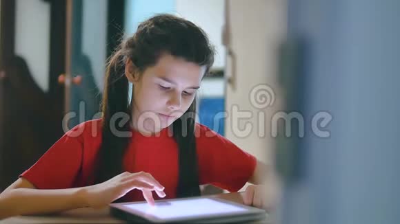 小女孩在玩数字平板电脑小女孩坐在桌子旁玩电子平板电脑在网上生活方式游戏视频的预览图