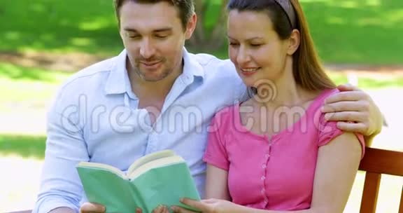 一对幸福的夫妇坐在公园的长椅上一起读书视频的预览图