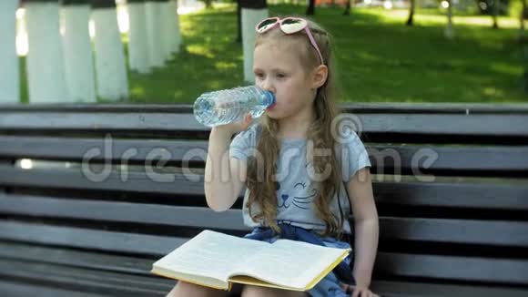 一个年轻女孩坐在城市的木凳上看书背景是一个城市公园视频的预览图