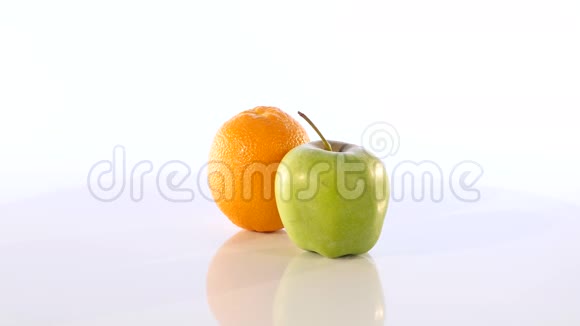 一个橘子和一个绿色的苹果水果在白色的背景上慢慢旋转视频的预览图