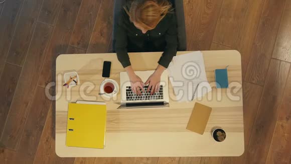 一个年轻漂亮的女人坐在桌子上在笔记本电脑上打字视频的预览图