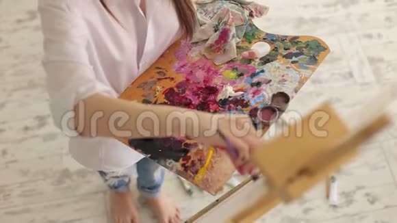 一个穿白色衬衫的年轻女孩在画室里画画布艺术视频的预览图