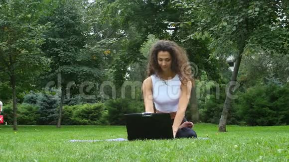 年轻女子在公园里用笔记本做瑜伽视频的预览图