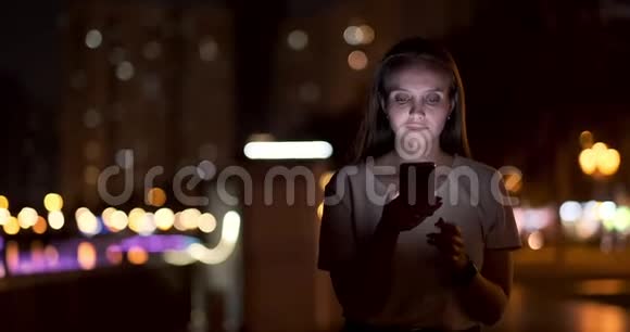 晚上一个年轻女孩手里拿着智能手机看着屏幕视频的预览图