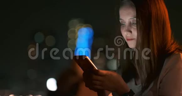 晚上一个年轻女孩手里拿着智能手机看着屏幕视频的预览图