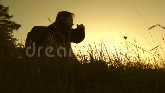 孤独的旅行者坐在山顶上在热水瓶里喝咖啡游客喝热茶看日落休息休息视频的预览图
