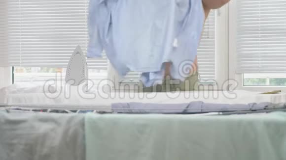年轻男子裸露的躯干站在板后使用蒸汽熨斗熨烫衬衫在家务4k慢镜头视频的预览图