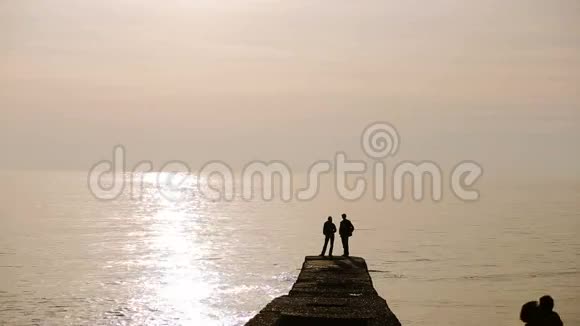 日落时分人们站在海边的码头上的剪影情侣相爱视频的预览图