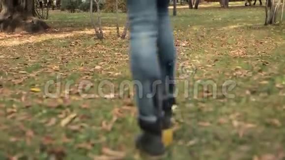 女人走在橙色叶子上的秋天公园里跟踪射击低角度视频的预览图