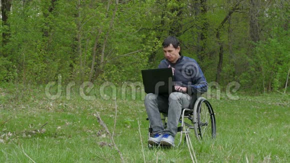 残疾人认为轮椅上的笔记本电脑有问题坐在轮椅上在自然绿色背景下工作视频的预览图