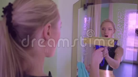 年轻漂亮的女人站在镜子前擦拭镜子视频的预览图
