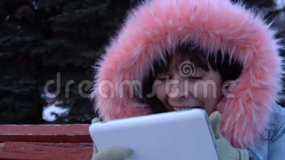 冬天一个穿暖和夹克的年轻女子在公园里使用数字平板电脑视频的预览图