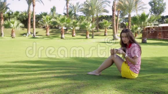 穿着黄色裙子坐在草地上打电话的年轻美女视频的预览图