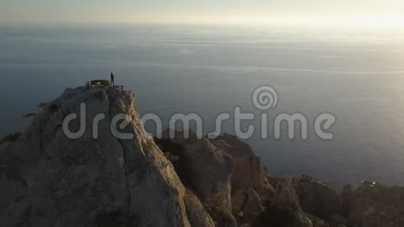 一位年轻女子站在一座面向大海的山顶上的鸟瞰图在美丽的风景中登上顶峰的女士视频的预览图