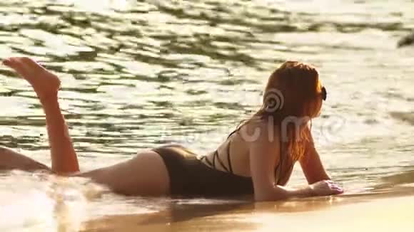 穿着黑色泳衣的金发女孩和白色沙滩上的黑色太阳镜有日光浴的漂亮模特视频的预览图