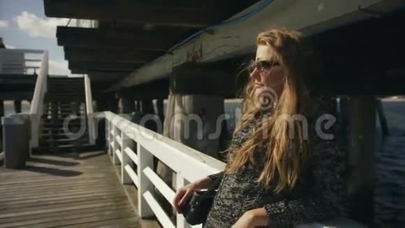 戴太阳镜的年轻女子站在海边的码头上视频的预览图