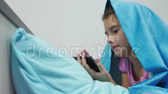 十几岁的女孩在毯子下玩智能手机小女孩睡前躺在床上上网室内视频的预览图