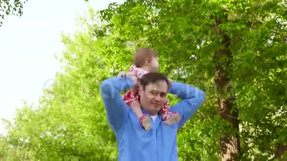 爸爸把小女儿扛在肩上带着孩子在夏季公园散步视频的预览图