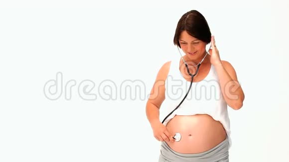 布鲁内特孕妇用听诊器倾听她的腹部视频的预览图