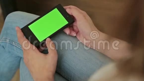 漂亮的女人手里拿着绿色屏幕显示的智能手机视频的预览图