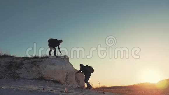 在两个登山者之间帮忙的剪影山顶上有两个徒步旅行者一个人帮助一个人爬上一个纯粹的地方视频的预览图