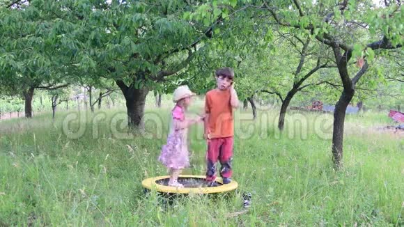 一个可爱的女孩在自然花园里跳舞小女孩在一个小蹦床上跳舞和跳跃小女孩穿花衣服视频的预览图