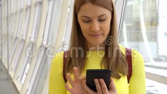 年轻漂亮的女人在商场里带着智能手机浏览互联网与朋友交流视频的预览图
