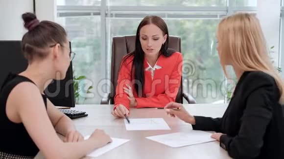 三个穿着商务套装的年轻漂亮女人坐在办公桌前讨论工作流程主管和下属视频的预览图