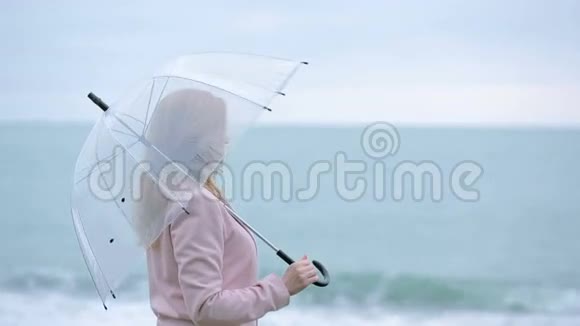 暴风雨中穿着粉红色外套带着透明雨伞的女孩在海边视频的预览图