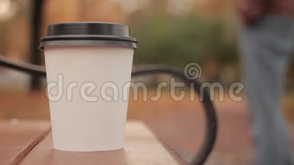 白色纸杯与热饮在秋天的城市公园接近离焦背景滑冰男孩行走的人视频的预览图