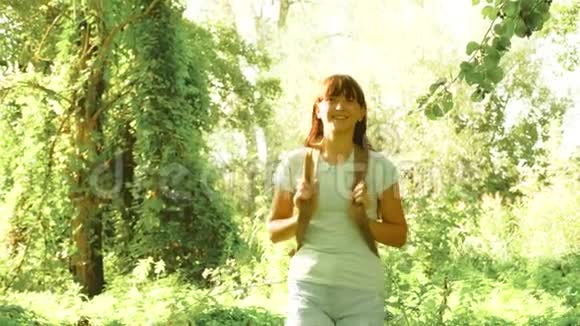 女旅行者带着背包在树林里散步夏天公园里快乐的徒步旅行者女孩少女冒险视频的预览图