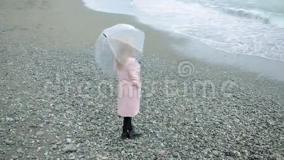 暴风雨中穿着粉红色外套带着透明雨伞的女孩在海边视频的预览图