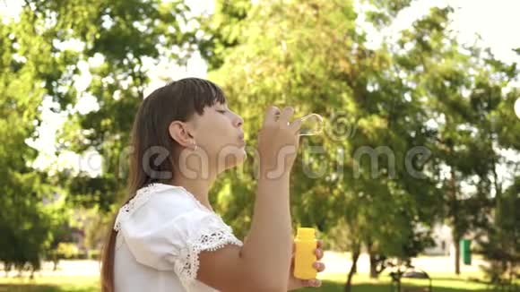 快乐的女孩在春天夏天和微笑的公园里吹着美丽的肥皂泡慢动作年轻女孩旅行视频的预览图