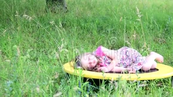 一个可爱的女孩在自然花园里跳舞小女孩在一个小蹦床上跳舞和跳跃小女孩穿花衣服视频的预览图