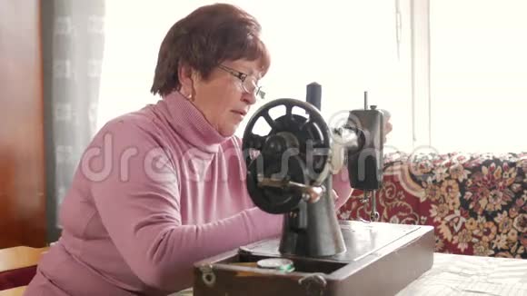 成年妇女在旧的手工缝纫机上缝纫眼镜穿着灰色布缝上视频的预览图