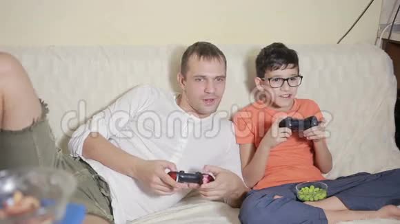 父亲和儿子在家里的沙发上玩电子游戏视频的预览图