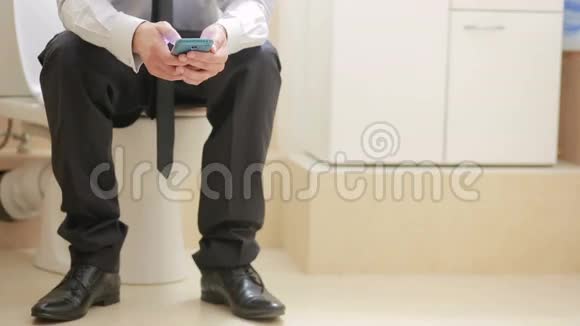 男商人坐在马桶上通过电话看新闻视频的预览图