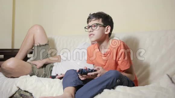 父亲和儿子在家里的沙发上玩电子游戏视频的预览图