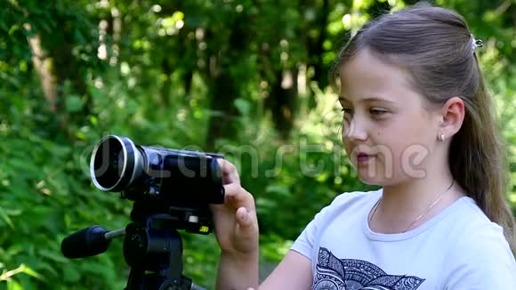 带着摄像机的年轻女孩在绿色公园慢动作拍摄电影视频的预览图