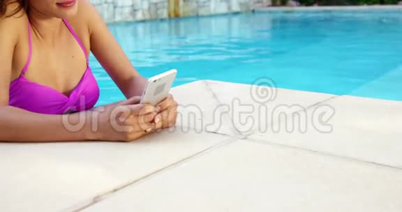 微笑的女人在游泳池放松使用智能手机视频的预览图