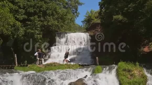 两位音乐家钢琴家和乐队演奏家在瀑布的岩石上演奏视频的预览图