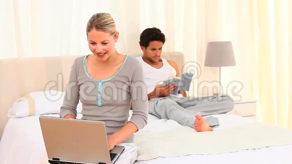 年轻夫妇带着笔记本电脑和一本书在床上视频的预览图